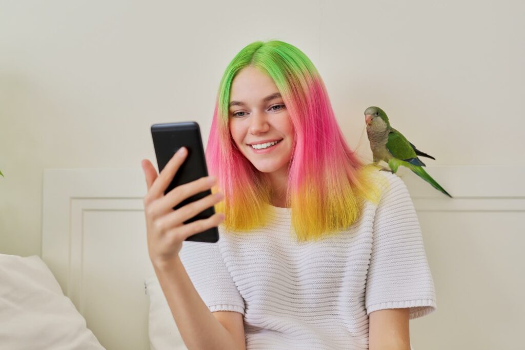 Trendy teen girl with smartphone and quaker parrot
